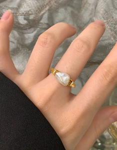 Detail of a gold irregular baroque pearl ring on a hand with minimalist styling