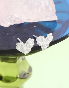 Macro shot of silver camellia heart stud earrings on a green glass holder