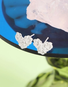 Close-up of S925 silver camellia heart earrings on a decorative blue glass tray