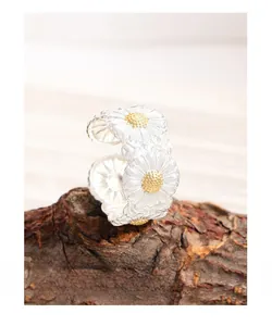 Detailed macro shot of S925 silver daisy rings on natural wood with gold center petals