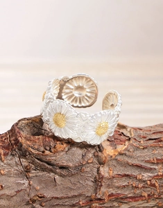 Close-up of S925 silver daisy ring with gold accents on rustic wood bark surface