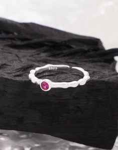 Macro detail of S925 silver ring featuring wavy texture and pink zircon on black charcoal