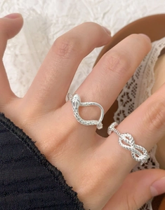 Macro shot of silver snake ring and twisted knot band showing detailed texture on hand