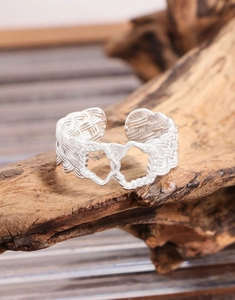 Macro view of woven silver ring featuring intertwined hearts on a natural wood surface
