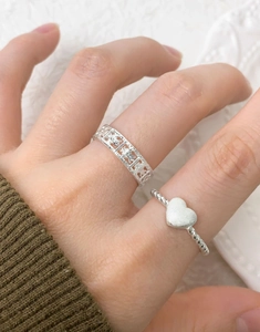Detail of twisted rope silver ring with matte heart and hollow patterned band on finger