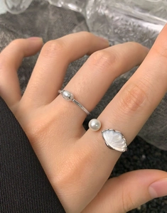 Dettaglio di anelli in argento S925 con perla e conchiglia sulla mano della modella
