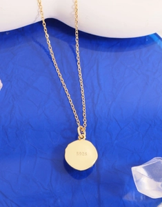 Close-up of S925 hallmark on gold plated irregular pendant with blue background