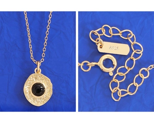 Macro detail of S925 sterling silver stamp and black agate pendant on a gold chain