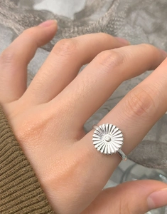 Close-up of a silver daisy flower ring worn on finger with soft knit sweater background