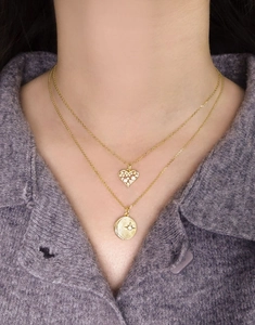 Close-up of double-layered gold star and moon pendant necklace on a purple sweater