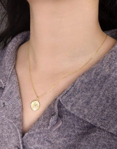 Close-up of golden sunburst pendant necklace with zircon on a purple knit background