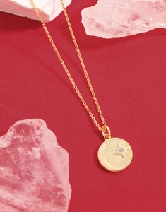 Macro detail of gold starburst necklace with central zircon on red textured background