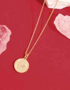 Detailed view of gold starburst engraved coin pendant with crystal on red background