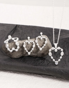 Detail of silver heart jewelry set with sparkling zircons on natural stone surface