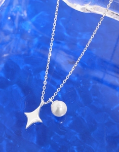 Macro shot of silver star charm and pearl pendant on a delicate chain against blue background