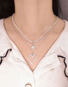 Close-up of layered silver necklace set with heart pendant and white pearl on model