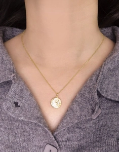 Detail view of a gold star and moon pendant necklace worn over a purple sweater