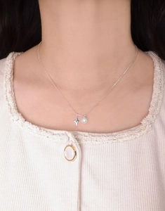 Detail of S925 silver star and pearl necklace worn by a model on a beige knit sweater