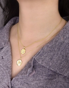 Detailed view of layered gold starburst necklaces on a model wearing a purple cardigan