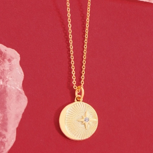 Golden S925 silver necklace with a starburst zircon round pendant on a red background