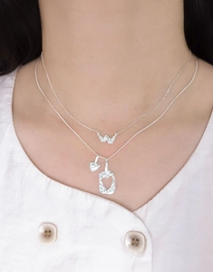 Détail d'un collier double en argent S925 avec pendentifs noeud et coeur martelé sur modèle