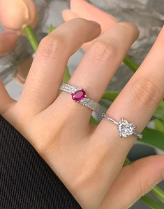 Detail of red oval zircon and heart-shaped gemstone ring on woman's fingers
