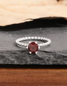 Detailed close-up of a twisted silver ring featuring a round red zircon on a stone surface
