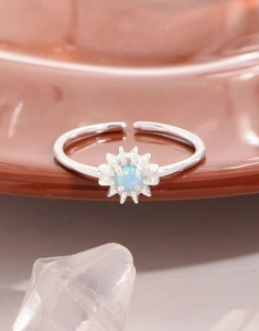 Makroaufnahme eines Gänseblümchen-Silberrings mit Opal-Zentrum auf Keramikfläche