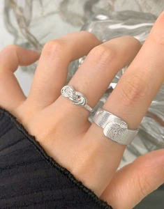 Dettaglio di anelli in argento 925 con nodo e trama larga indossati su un dito femminile