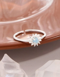 Makro-Detail des silbernen Gänseblümchen-Opal-Rings auf Keramik mit Kristall