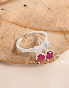 Macro view of S925 silver cherry bow ring with red gemstones on a natural dried leaf