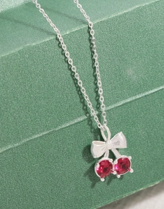 Macro de pendentif cerise en argent avec oxydes de zirconium rouges et nœud sur fond vert