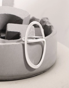 Macro shot of polished S925 silver irregular ribbon ring on minimalist grey concrete base