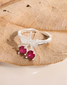 Detailed close-up of cherry bow silver ring with red stones on a natural leaf base
