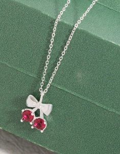 Détail du collier en argent S925 avec pendentif cerise et nœud sur boîte en cuir vert