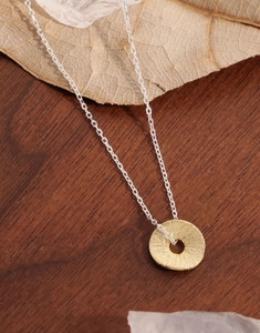 Macro detail of a silver necklace featuring a textured golden coin pendant on wood