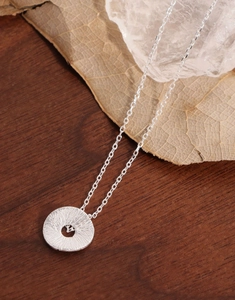 Macro shot of silver textured round pendant necklace on natural wooden background