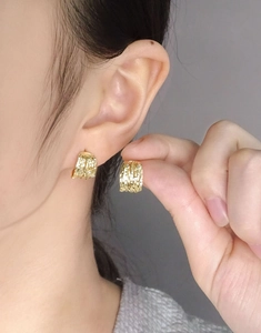 Close-up of gold C-shaped earrings with textured coil design and sparkling zircons