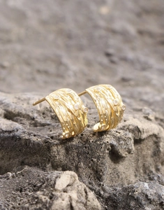 Macro shot of gold coiled zircon stud earrings on a natural grey textured stone