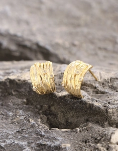 Close-up of irregular gold coiled line earrings with zircons on a gray stone surface