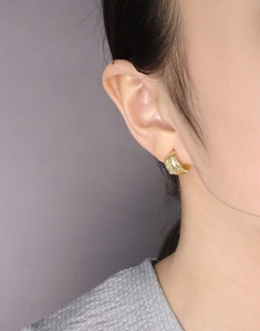 Detailed view of gold C-shaped earrings with irregular wavy texture on a model
