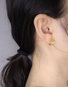 Close-up of gold irregular coiled line stud earrings with zircon inlay on ear