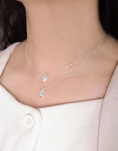 Detail of S925 silver layered necklace with star, pearl and bow charms on model neckline