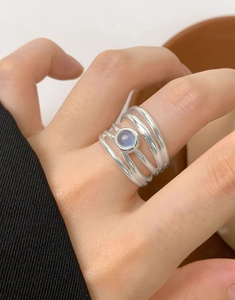 Close-up of a multi-layer silver ring featuring a round pale violet gemstone on a finger