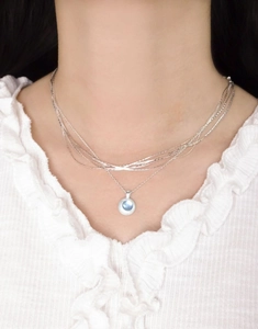Detail of layered S925 silver necklace with a round translucent blue gemstone pendant