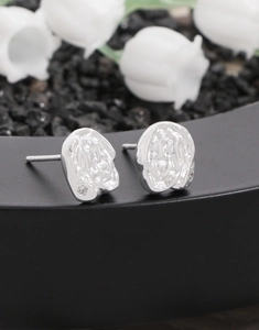 Macro shot of silver studs with lava texture, irregular metal folds and a clear zircon