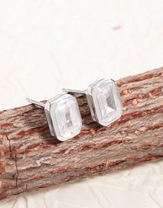 Detailed close-up of emerald-cut zircon earrings on a natural wooden branch display