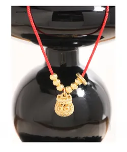 Detailed close-up of golden hollow money bag pendant on a red braided rope necklace