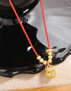 Detailed close-up of a golden money bag pendant on a red braided drawstring bracelet