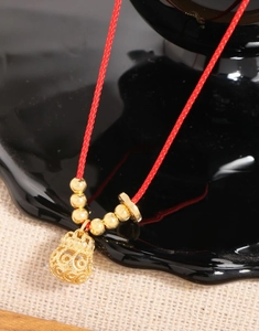 Detailed macro view of an intricate hollow gold money bag pendant on a red braided cord